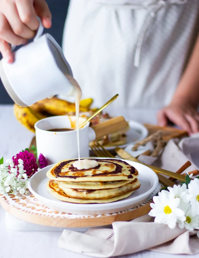 A hand pouring cream cheese icing over a pancake