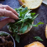 A hand placing some greens over the onions on the bread