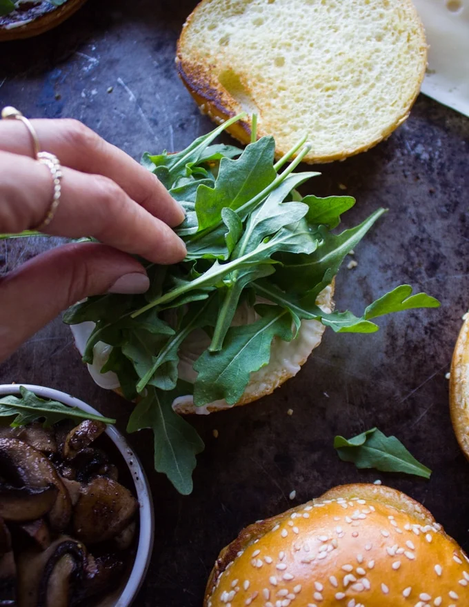 A hand placing some greens over the onions on the bread