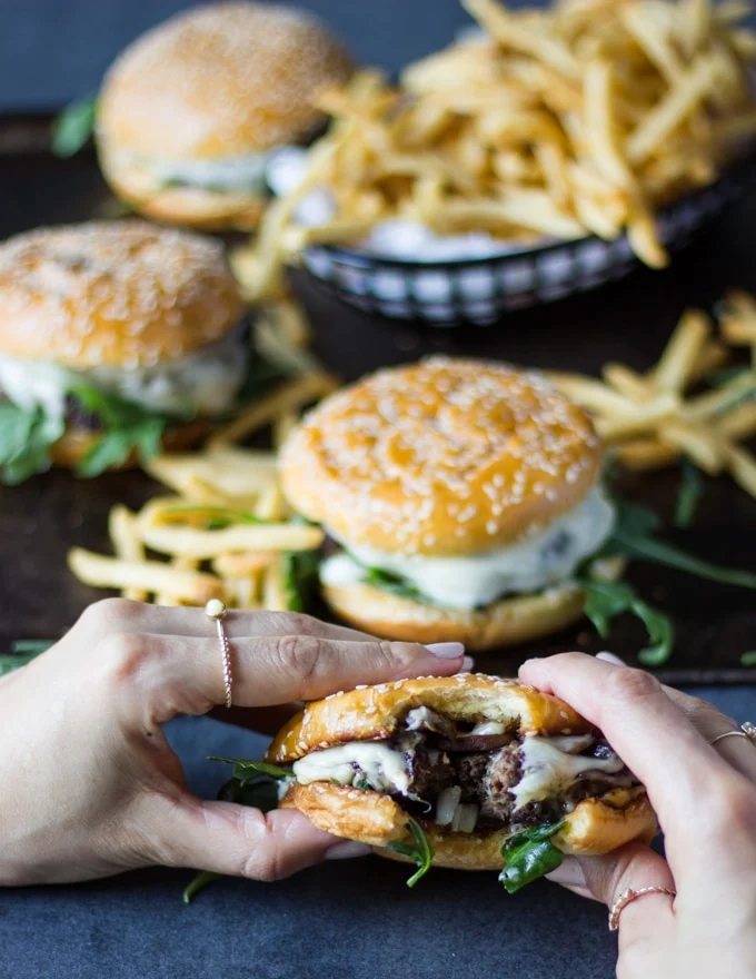 two hands holding on to a bitten mushroom swiss burger recipe from the tray showing other burgers around it.