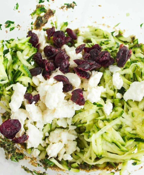 grated zucchini, dried cranberries and feta being added to the zucchini fritter batter
