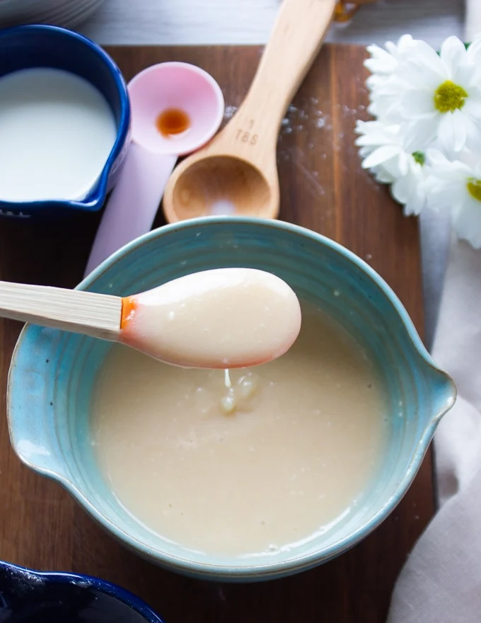 Cream cheese icing in a bowl and a spatula dripping it over the plate showing the smooth consistency