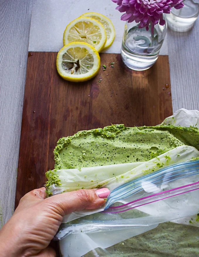 A hand holding the opened bag of frozen pesto showing the texture
