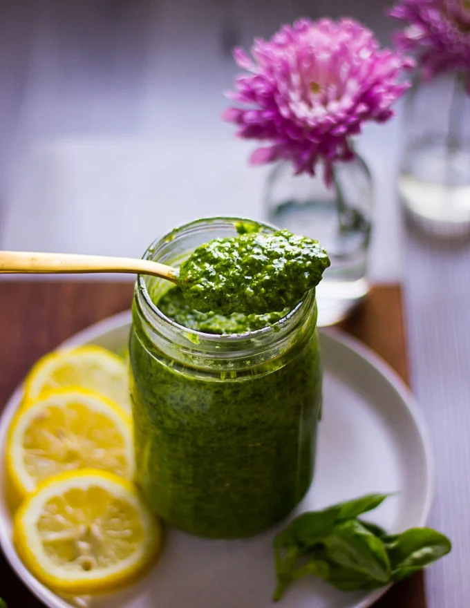 A spoon holding a spoonful of basil pesto over a jar of pesto
