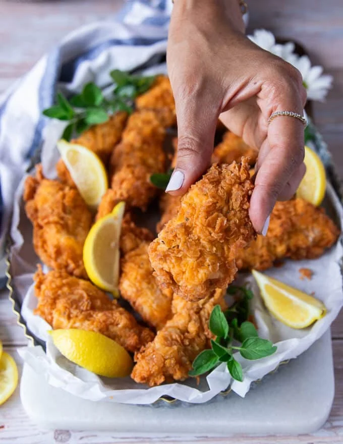 A hand holding a piece of chicken fingers close up showing the texture and crunch of the cooked chicken