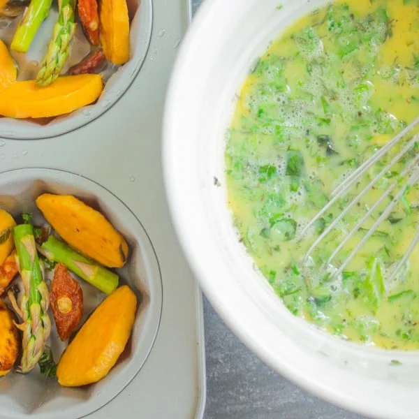 pan-fried vegetables in a muffin pan waiting to be topped with herb-speckled frittata batter.