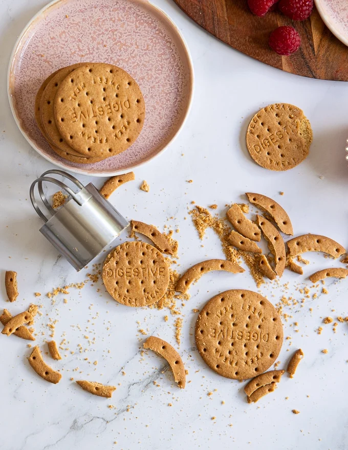 A cookie cutter cutting off cookies to fit the bottom of the cheesecakes