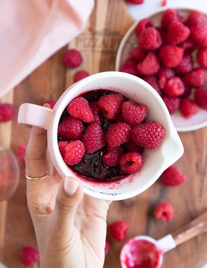 a hand showing close up of the fresh raspberries added to the raspberry jam