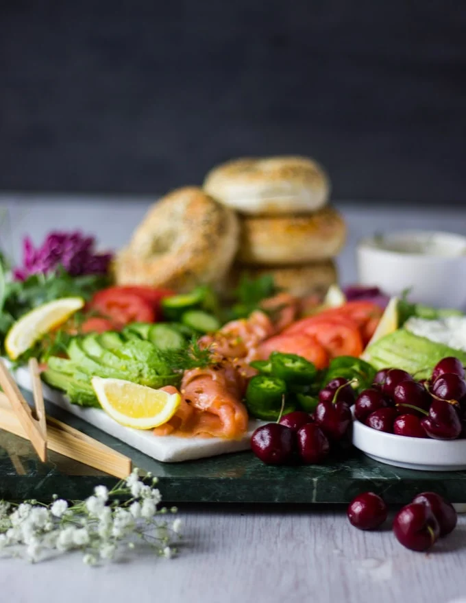 Side view of the assembled smoked salmon platter showing the fruits and avocados in focus and bagels in the background