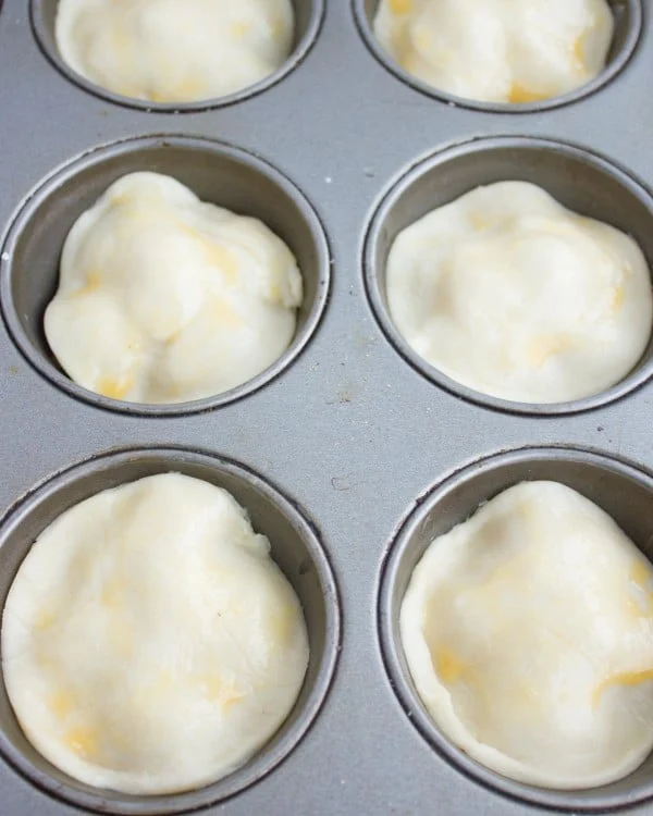 rounds of raw pastry dough placed on top of mini tomatoes for making tarte tatin in a muffins pan.