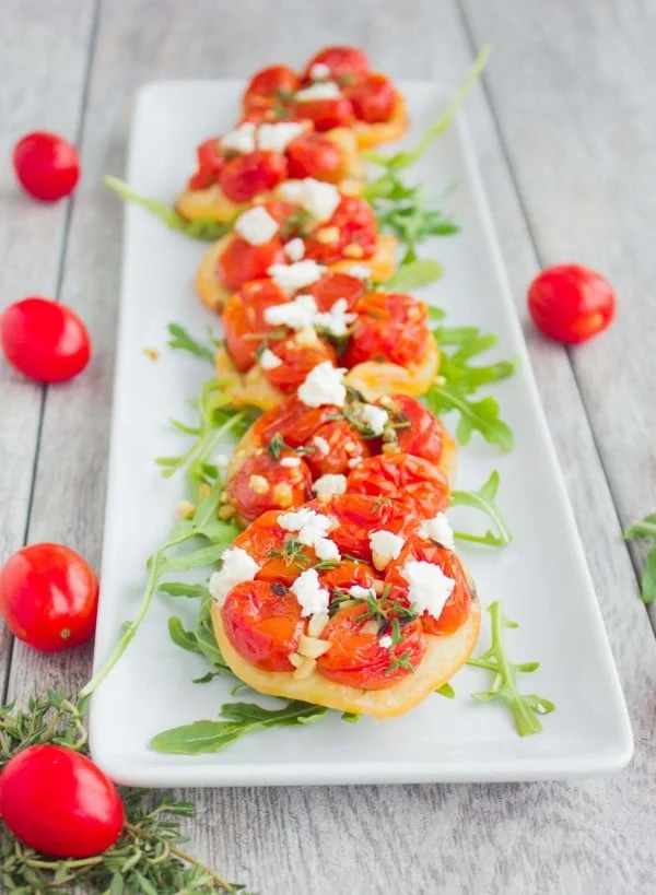 Mini Tomato Tartes Tatin decorated with some arugula and lined up on a while rectangular plate.