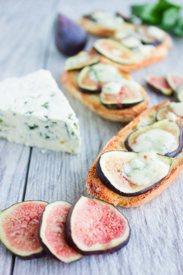 Fig Blue Cheese Honey Crostini drizzled with honey, served on a rustic table with a wedge of blue cheese and some figs in the background