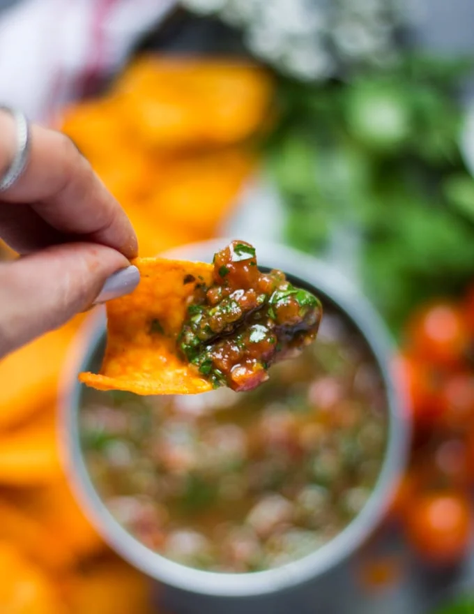 A hand holding a chip dipped in homemade salsa showing the texture