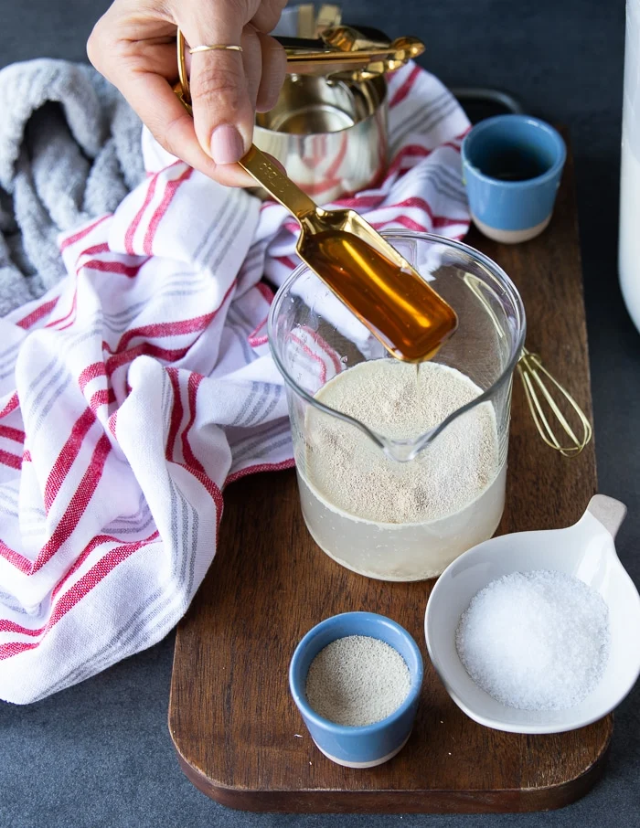 Pouring honey into a cup with warm water and yeast to proof the yeast.