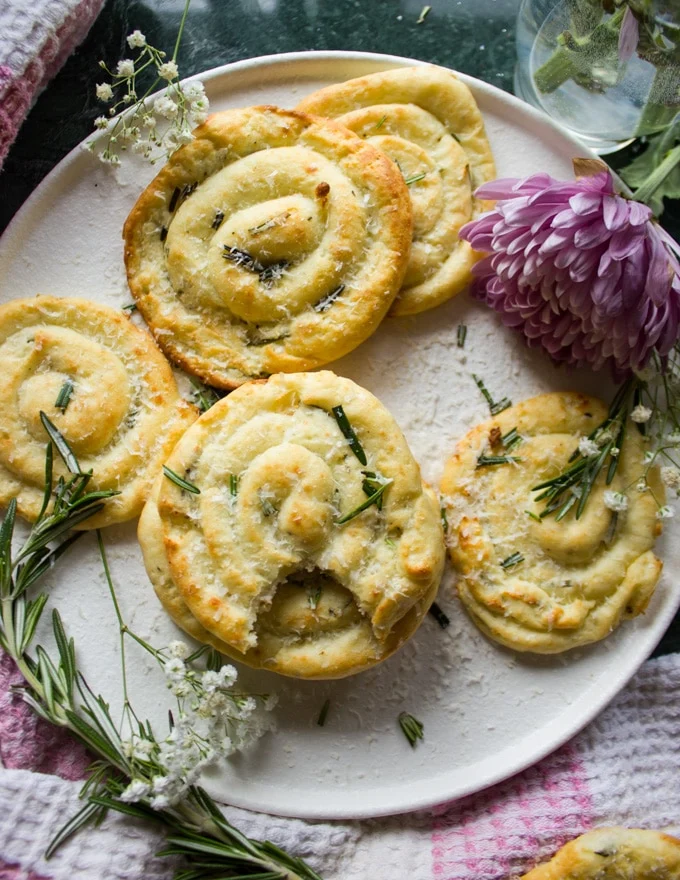 A plate with mashed potato pancakes with a fresh sprig of rosemary and flowers