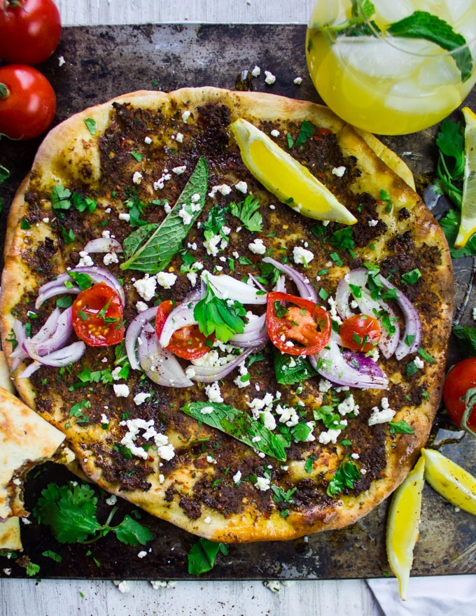 close up of a turkish piza lahmacun topped with herbs, tomatoes, onions, lemon slices and feta cheese