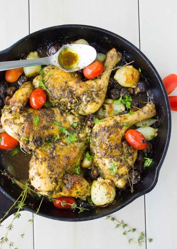 Butterflied Garlic Herb Roast Chicken served in a black skillet with some pearl onions, mushrooms, blistered tomatoes and fresh herbs