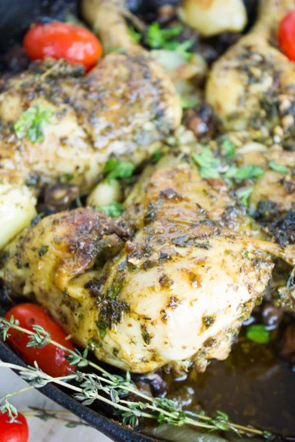 Butterflied Garlic Herb Roast Chicken served in a black skillet with some onions, mushrooms, blistered tomatoes and fresh herbs