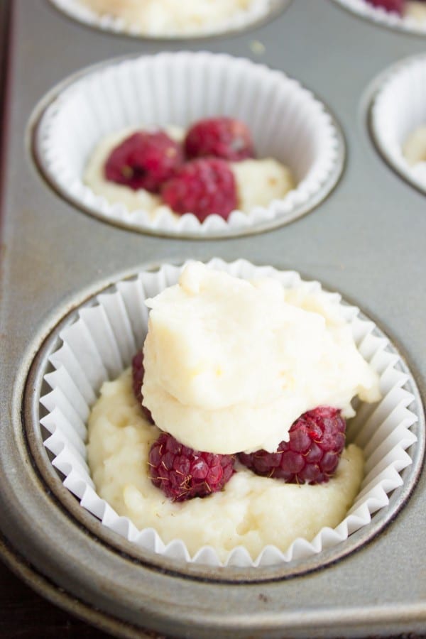 close-up of a tray of unbaked muffins with fresh raspberries peaking out of the batter.