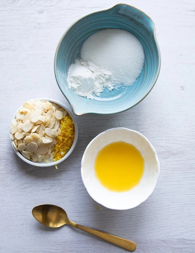 ingredients for the lemon toppings crunchy toping for raspberry muffins rercipe including a bowl of butter, bowl of sugar, lemon zest, sliced almonds and a spoon