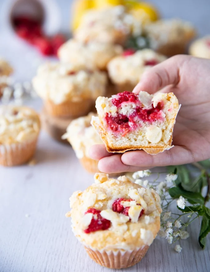 A hand holding a raspberry uffin cut in half showing the inside of the fluffy raspberry muffin recipe and fresh raspberries not mushed.