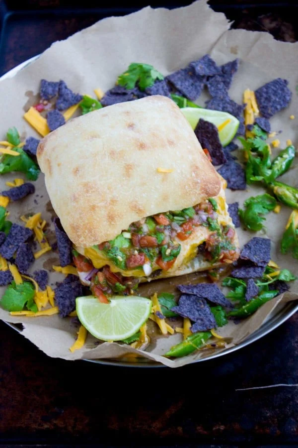 top view of the juicy burger loaded with fajita toppings served on a tray with tortilla chips and lime wedges
