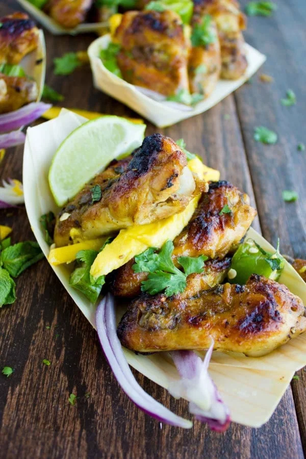 close-up of a serving of sweet and spicy chicken wings smothered in mango chutney, served in a small oval paper boat