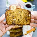 A hand holding a slice of whole wheat banana bread close up showing the airy texture, chocolate chunks and pecans