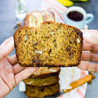A hand holding a slice of whole wheat banana bread close up showing the airy texture, chocolate chunks and pecans