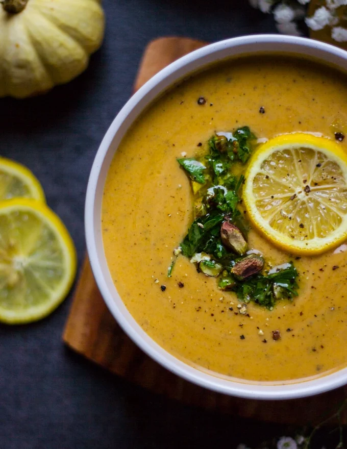 A half a bowl of Mediterranean soup or autumn squash soup toped with lemon slice and crunchy pistachio and parsley