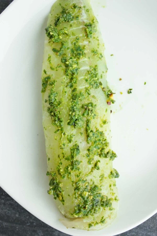 white fish fillet coated with green pesto on a white plate.