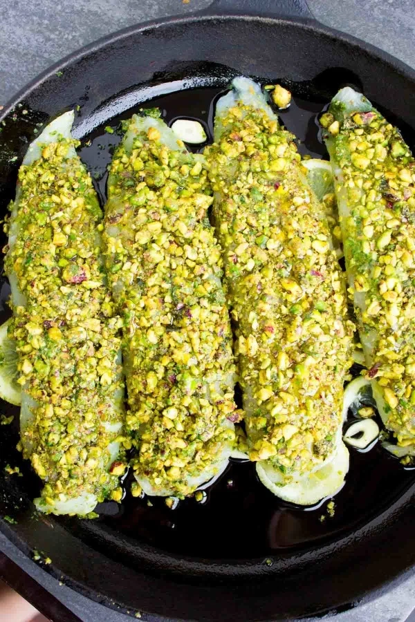 Four Pesto Pistachio Fish Fillets neatly lined up in a black skillet ready for the oven.