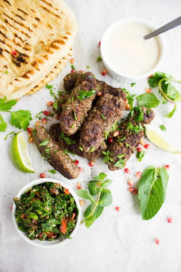 Top view of lamb kebabs grilled, some tahini sauce on the side, tabouleh salad and fresh mint