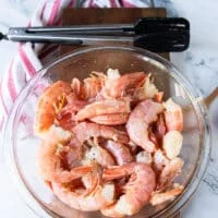 Raw shrimp in a bowl with salt, pepper and olive oil