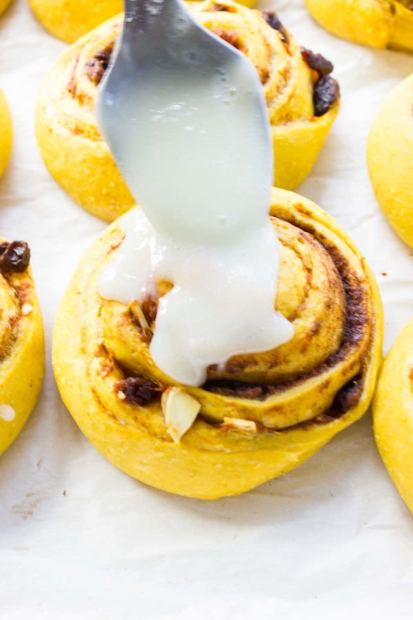 Pumpkin Cinnamon Roll being glazed with cream cheese frosting