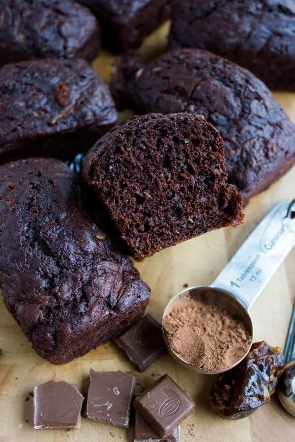 mini loafs of Double Chocolate Date Zucchini Bread on a wooden board with some dates and cocoa powder on the side.