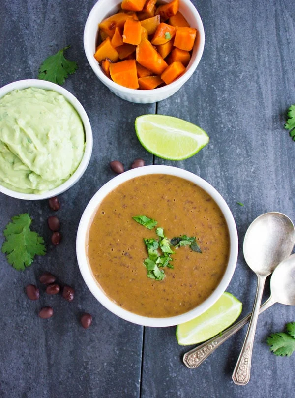 a bowl of Sweet Potato Black Bean Soup with avocado crema and roasted sweet potato cubes on the side