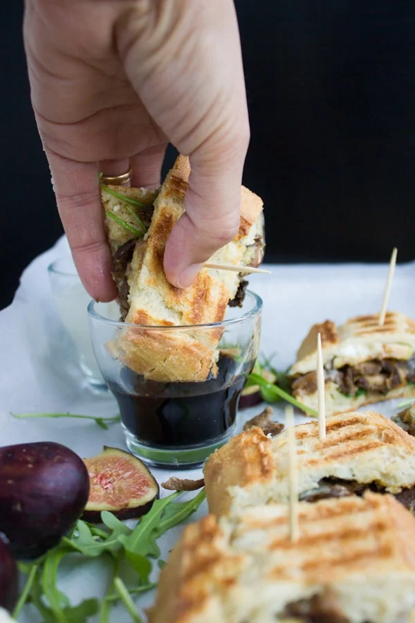Slice of Blue Cheese Philly Steak Sandwich being dipped into a dish with balsamic dip