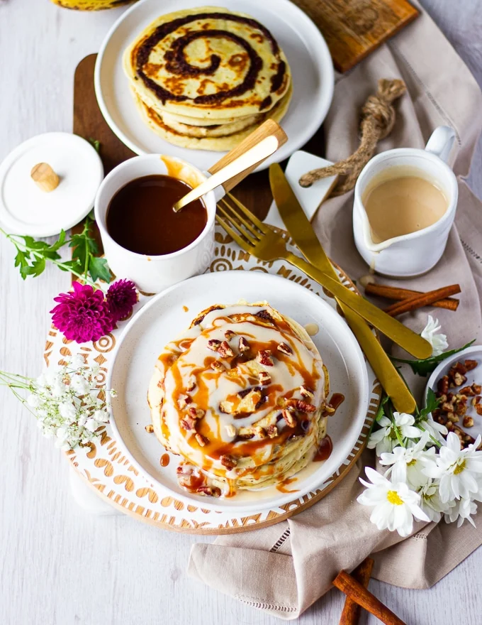 top view of cinnamon rolls pancakes and all the sauces including caramel sauce and cream cheese icing and nuts and some coffee