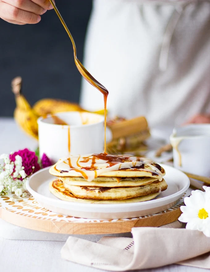 A hand drizzling caramel sauce over the pancakes