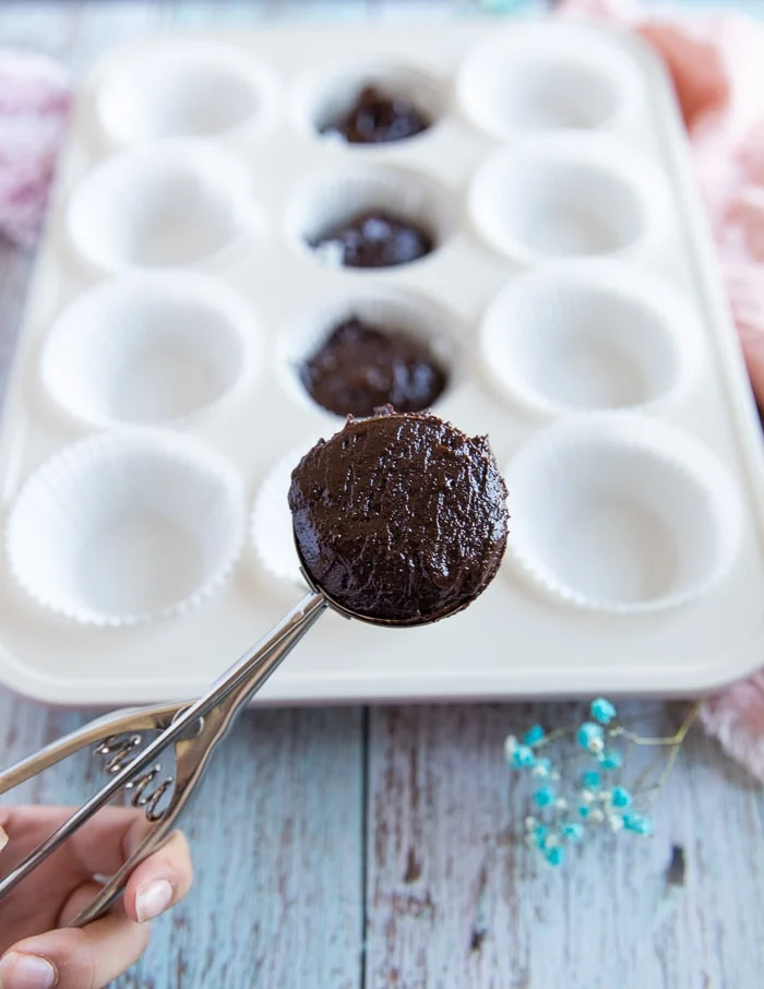An ice cream scoop holding coconut brownie batter to place into the baking pan
