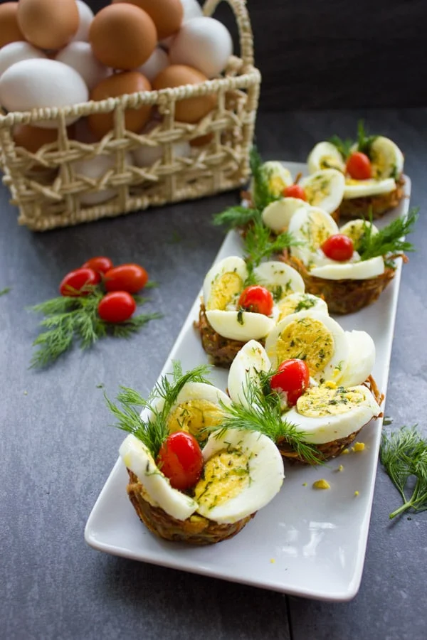 Easter Egg Tart Potato Nests on a rectangular white plate topped with eggs, tomatoes and fresh dill