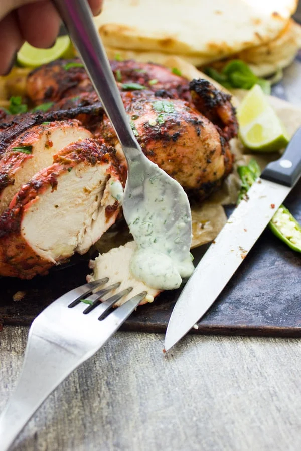 a piece of Quick Roast Tandoori Chicken being drizzled with yogurt sauce