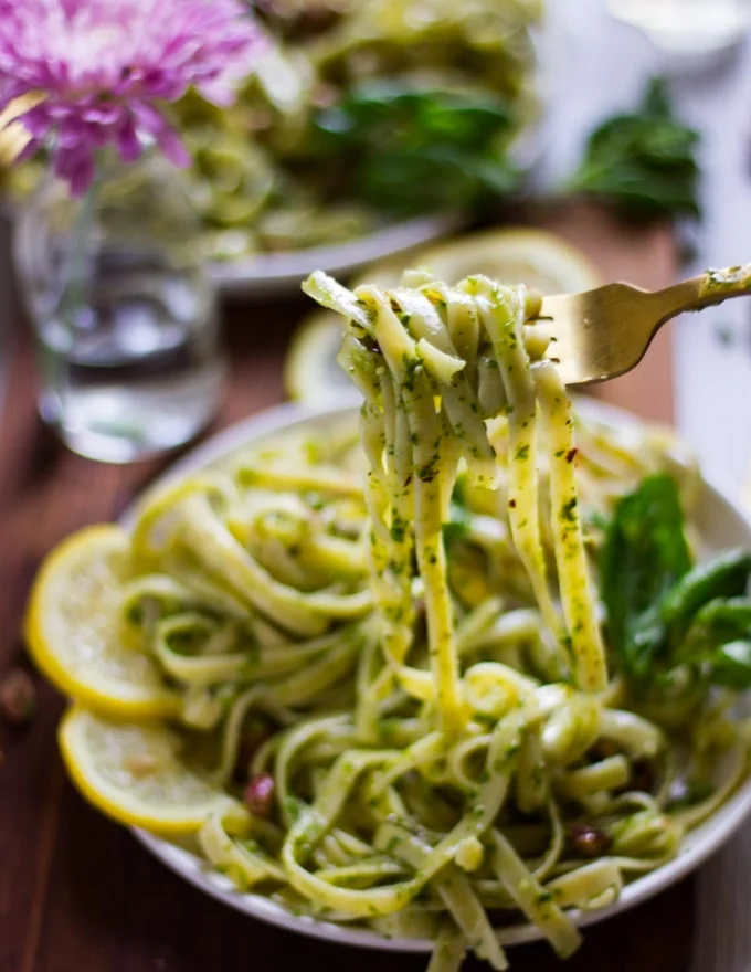a fork stretching out some pesto pasta to show the specs of pistachio pesto over the pasta