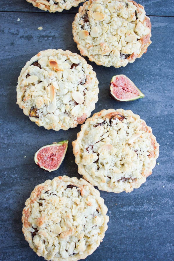 overhead shot of Individual Fig Almond Frangipane Tarts arranged on a rustic dark tabletop