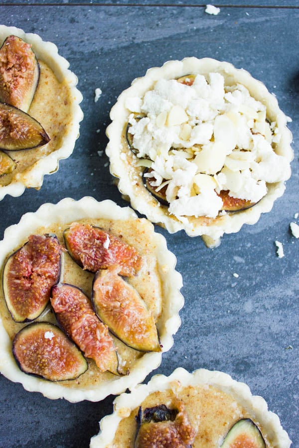 almond frangipane tarts being topped with fresh fig slices and almond streusel topping