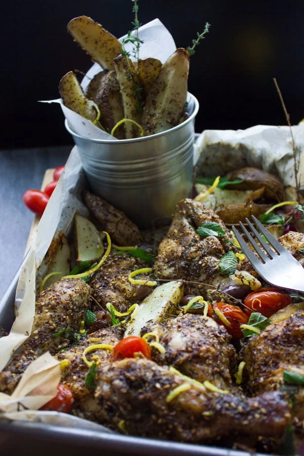 One Pan Chicken Potato Bake topped with Zaatar, lemon zest and roasted tomatoes on a silver baking tray