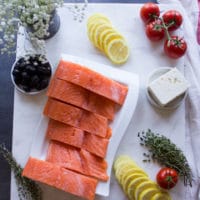Ingredients for Baked Salmon with Greek Dressing: fish, tomatoes, lemon, feta, olives, herbs.