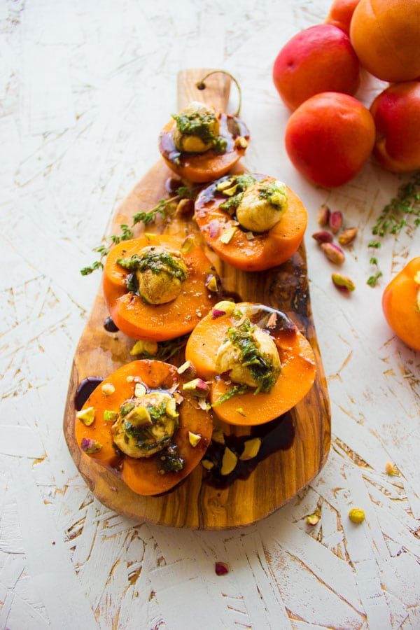 overhead shot of a wooden board with 4 apricot halves stuffed with mozzarella and pistachios