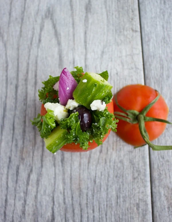 overhead shot of a hollowed out tomato being stuffed with Kale Greek Salad